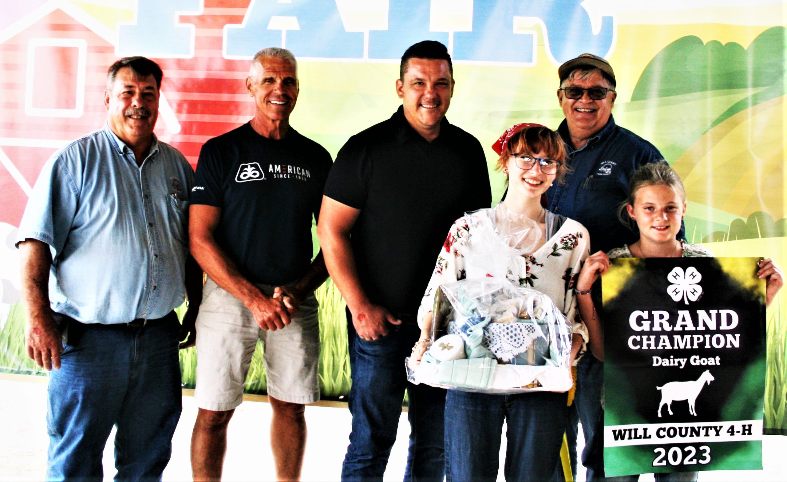 Reganne Price had the grand champion goat at this year’s Will County Fair, and the Will County Farm Bureau purchased a gift basket of goat items for her hard work. Pictured from left, Steve Warrick Sr., Dave Kestel, Brad Metzger, Reganne Price, Mark Schneidewind, and assisting Reganne holding the sign was Bentley Bourdreau. (Submitted photo)