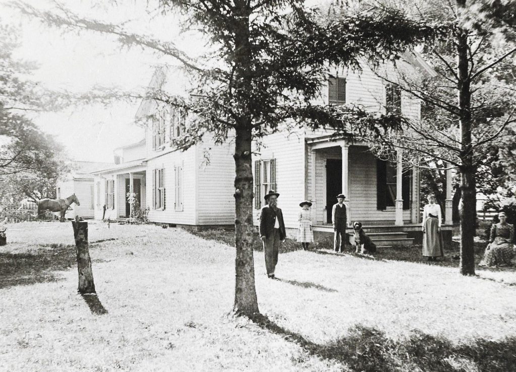 This picture was taken around 1890 based on age of Doug Gougar's grandfather, Harlow Gougar, who is standing next to the dog. He was born in 1878. This picture shows his great grandfather, Joseph Emerson Gougar, at the left behind the tree. He was born in 1834 and was the 11th child (and a twin) of William Gougar Sr. who settled at the Gougar Crossing (Route 30 and Gougar Road) in 1830. He was one of the first five settlers in the area, which later became Will County. Joseph Emerson bought 160 acres off a dirt path 1 3/4 miles south of the original homestead in 1860. That dirt path later became Gougar Road, where the Gougar Farm is now. Standing to the right and behind Joseph Emerson is daughter Eva Agnes Gougar, a son, Harlow Webster Gougar (Doug's) grandfather), another daughter Harriet May Gougar, and wife, Hattie Gougar (sitting). They had two other daughters who died in infancy. They also had another son, Charlie Gougar, who passed away at a young age. The house pictured still stands today much the same as it was when built in 1864, and is still home to the existing Gougar family who maintains and runs the farm. 