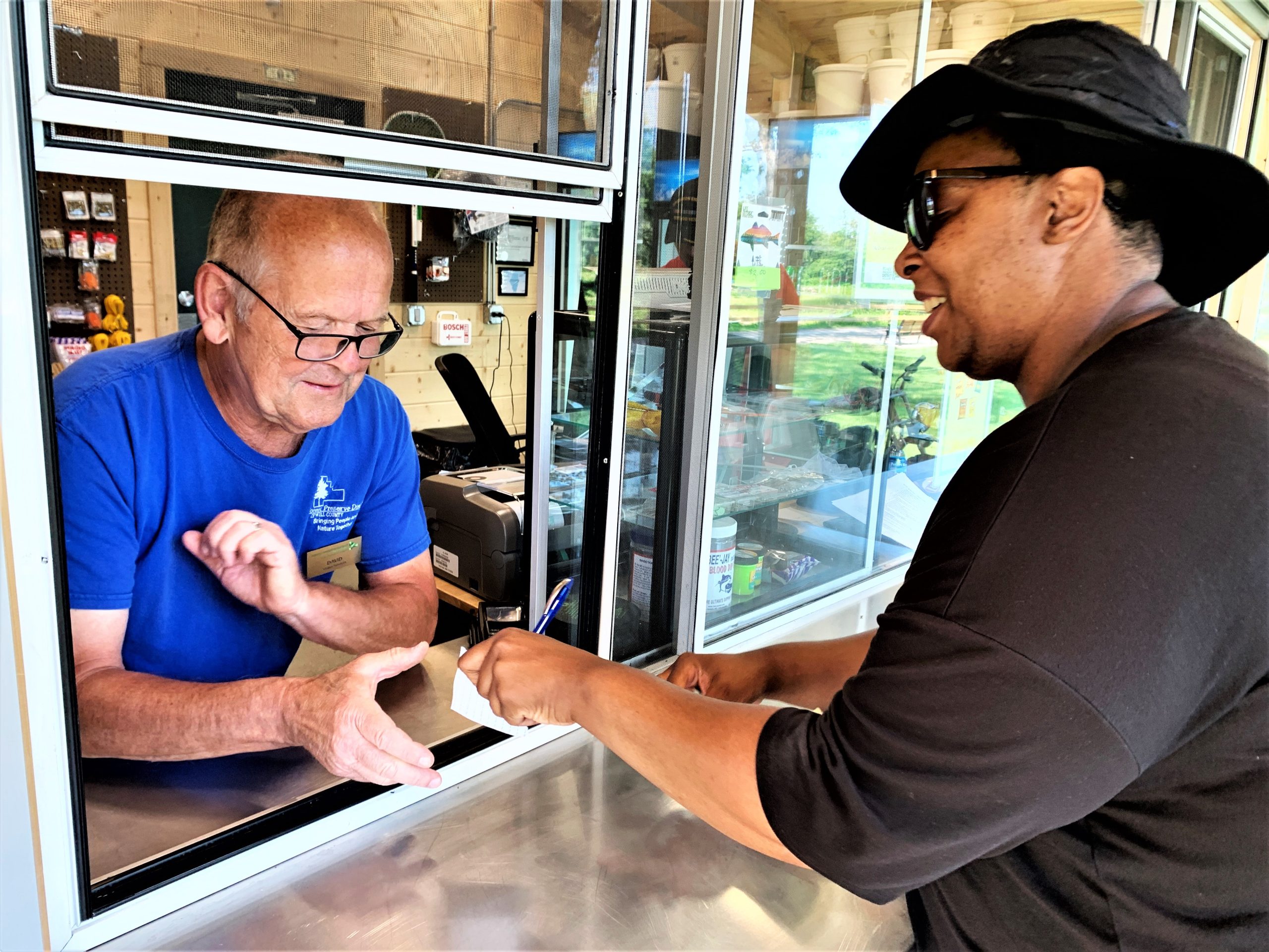 Forest Preserve District of Will County employee David Piotrowski sells a carton of water to Naperville resident Angela Karellas at the new Tackle Box bait shop at Hidden Lakes Trout Farm in Bolingbrook.(Photo by Forest Preserve staff | Cindy Cain)