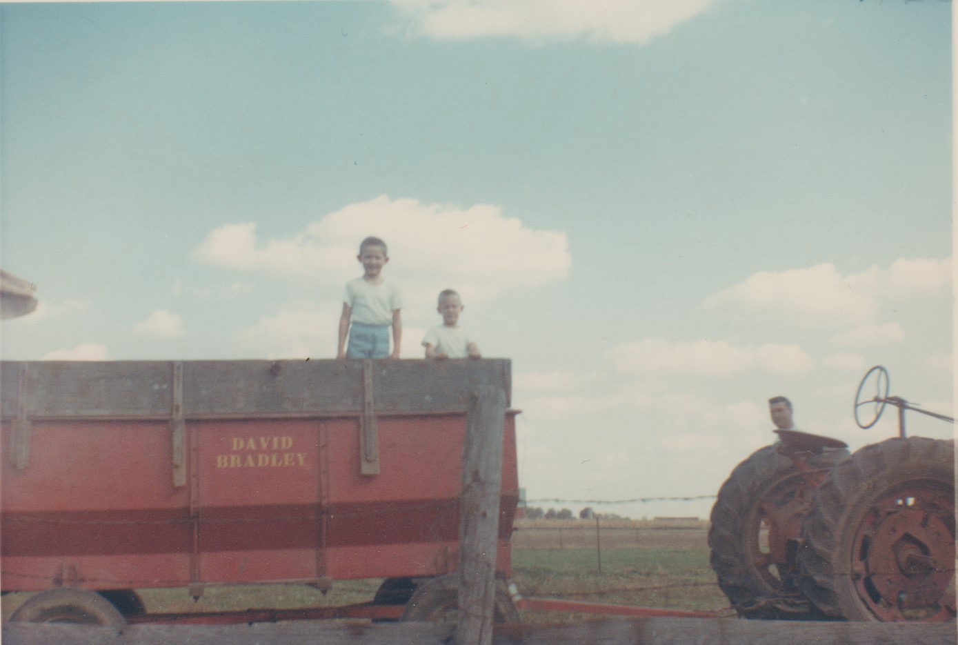 Brothers Rodney and Ron Bettenhausen (ages 6 and 4) standing in a wagon load of corn while their father, Rodger Bettenhausen, stands near the 1939 Farmall H tractor on the farm of their grandfather, Fred Bettenhausen of rural Manhattan in October 1965.