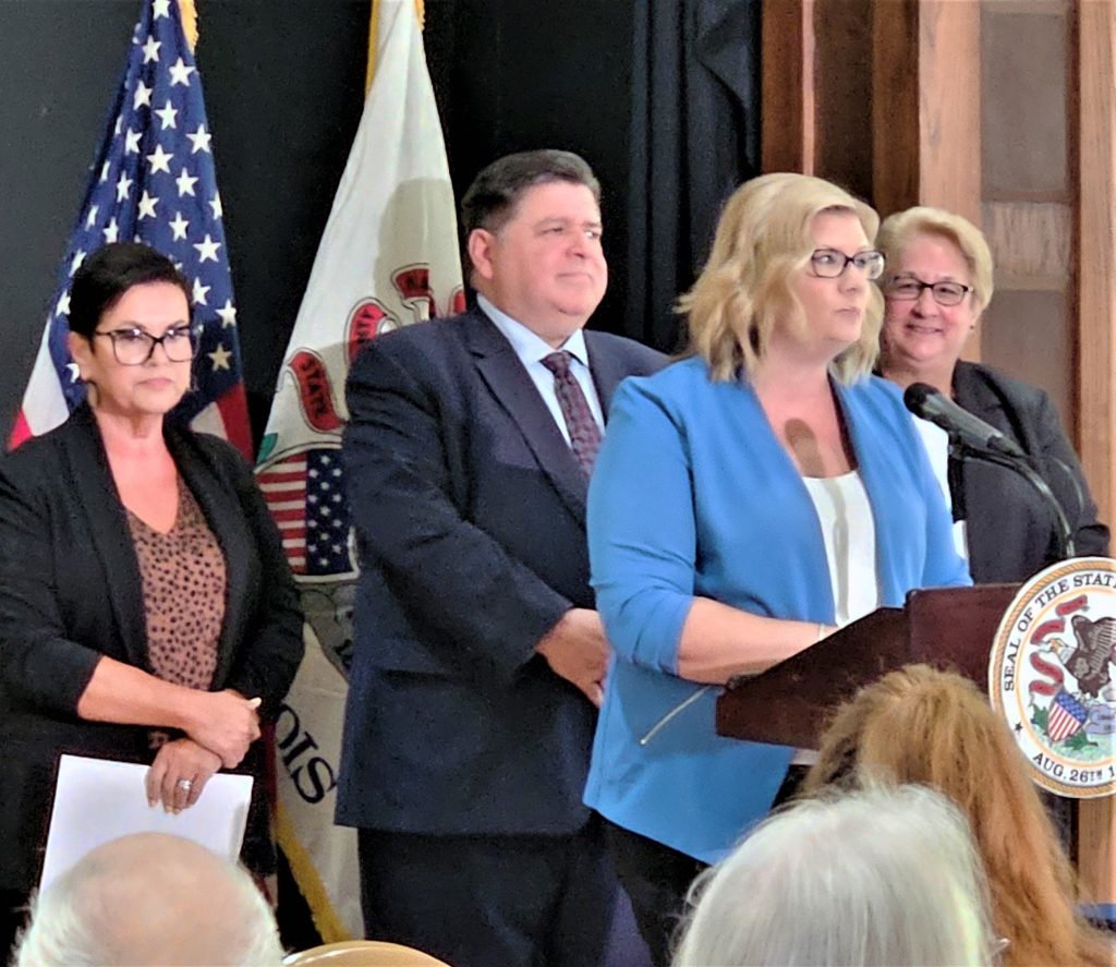 Brianne Hetmen, CEO of Senior Services of Will County, tells how a new pilot program in the county will help elderly relatives raising children find the resources they need to make life easier for them and the children. The bill was sponsored by state Rep. Natalie Manley, left, and signed by Gov. JB Pritzker during the ceremony. To the right is Paula Basta, Director of the state Department on Aging, which will oversee the program.