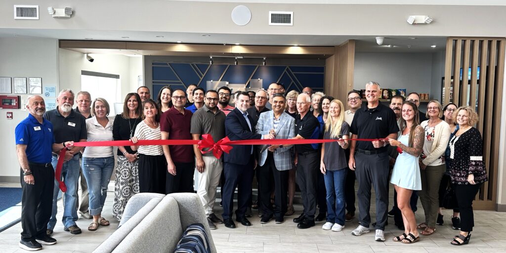 During the one-year celebration, Holiday Inn Express Manager Tom Forbes and owner Suhas Patel hold the ceremonial scissors while surrounded by members of the Chamber of Commerce, business leaders, Patel’s associates, employees and members of the Village Board and administration.(Photo by Andrea Arens)