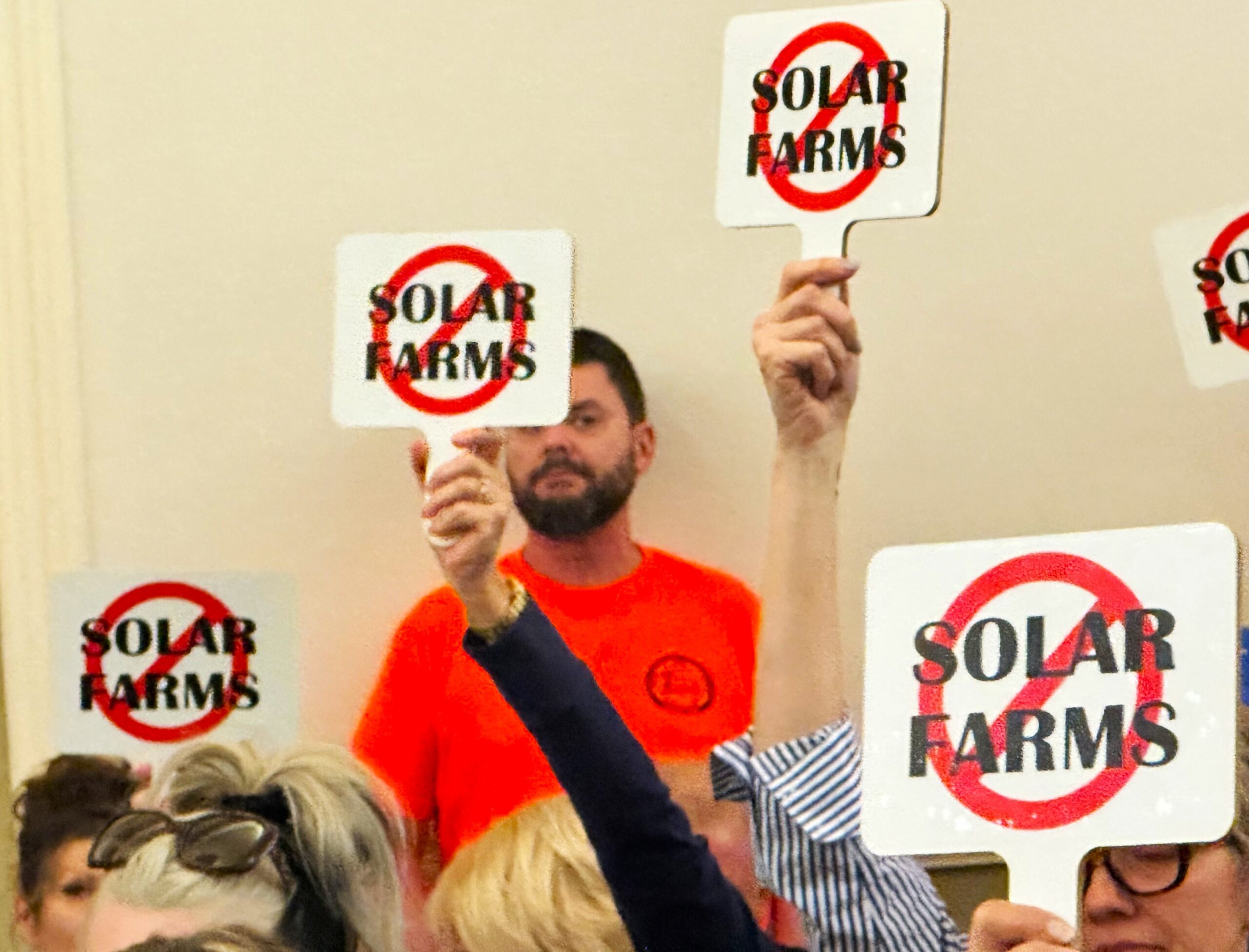 "No Solar Farms" signs were held up at Will County Planning and Zoning Commission hearings on Earthrise Energy's nearly 6,100-acre Pride of the Prairie solar farm plan every time a union member wearing orange spoke. The commission voted 4-2 to reject the plan. (Photo by Andrea Arens)