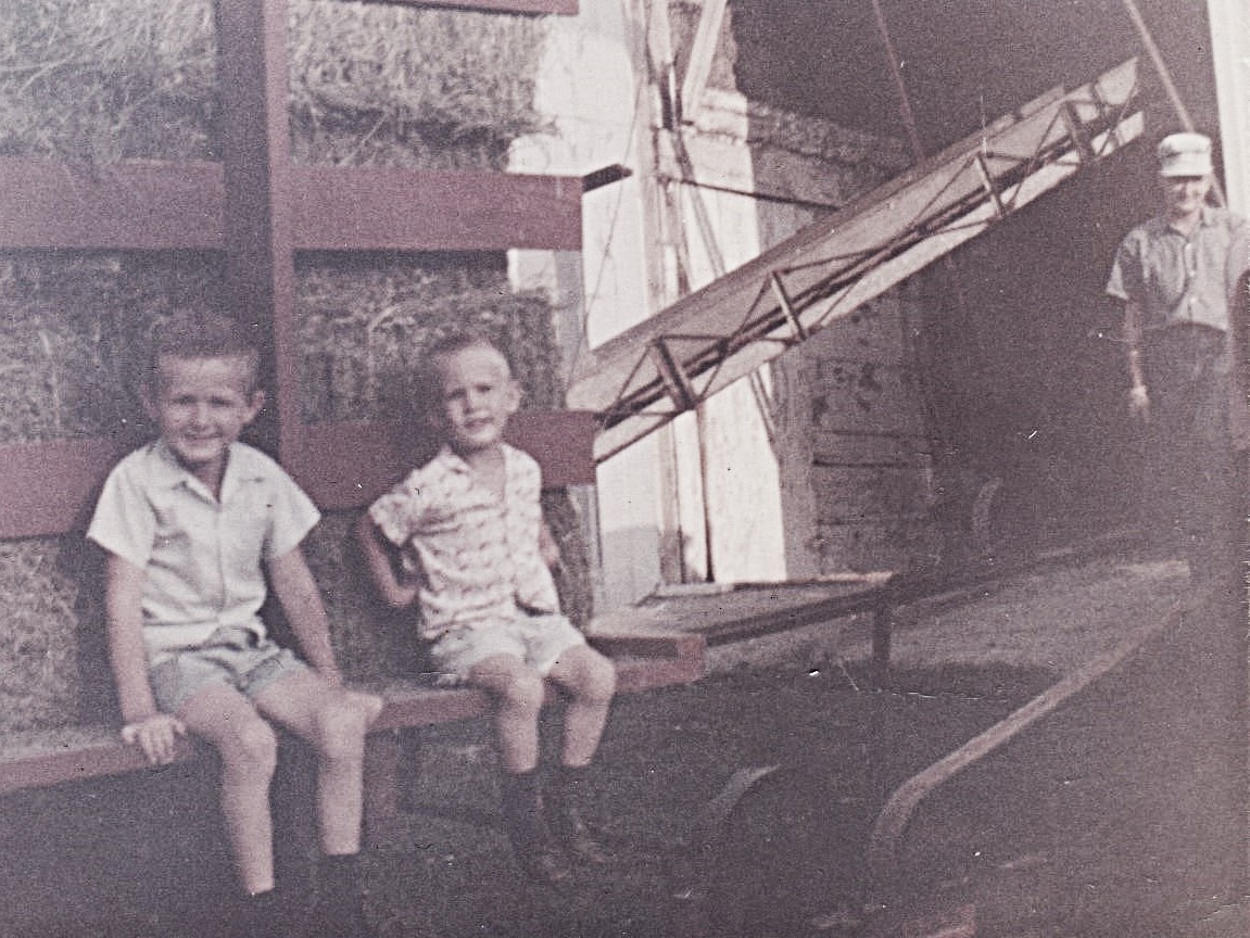 Brothers Rodney and Ron Bettenhausen (ages 5 and 3) sitting on a hay rack as it is unloaded into the barn by their grandfather, Fred Bettenhausen, standing near barn in July 1964. Rodney & Ron were visiting from New Lenox and always loved their grandfather's farm.